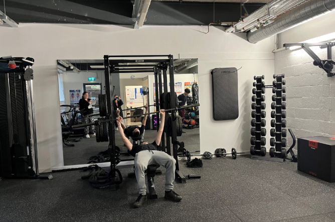 Image: boy in grey tracksuit on bench press, lifting weights