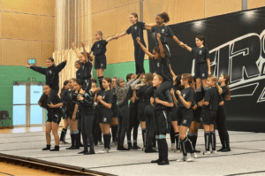 girls in black cheerleading outfits smiling and lifting 6 students in school gym