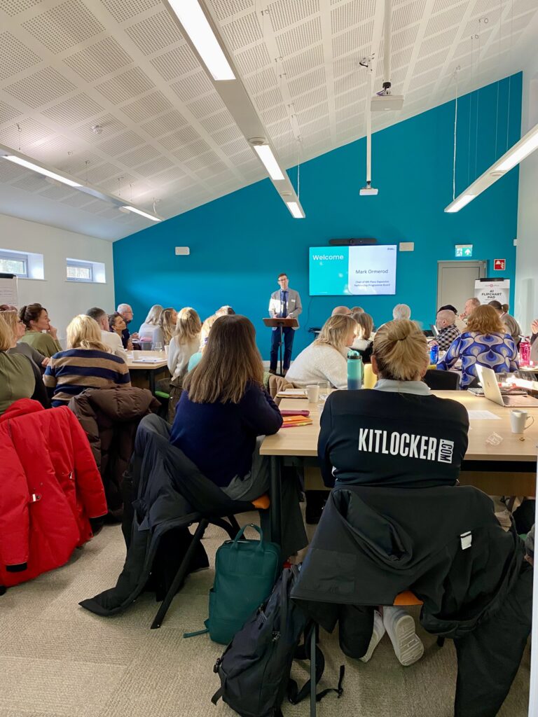 Group of people seated at tables looking towards speaker at front of room