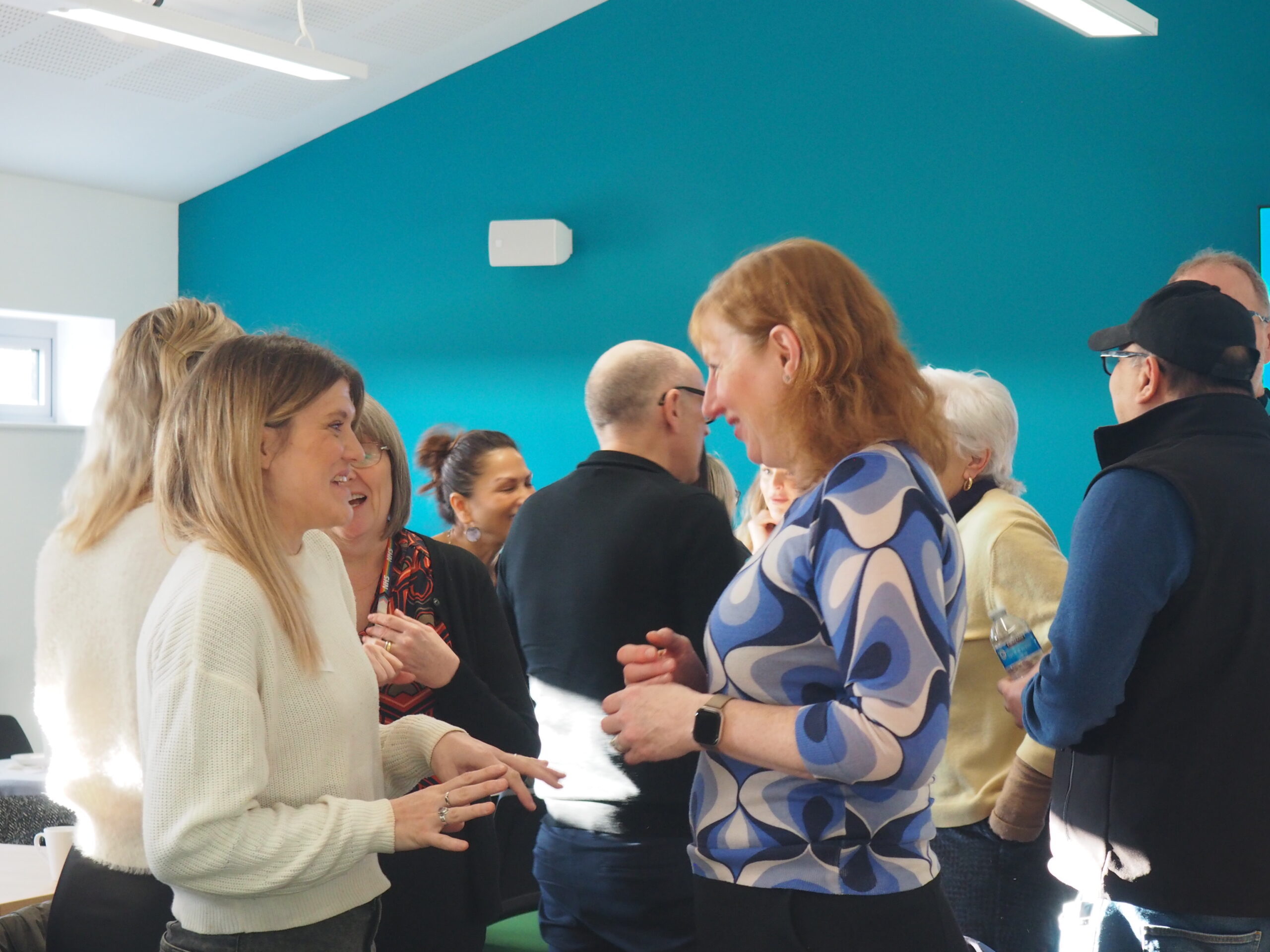 Room of people in conversations, focus on two people speaking to each other