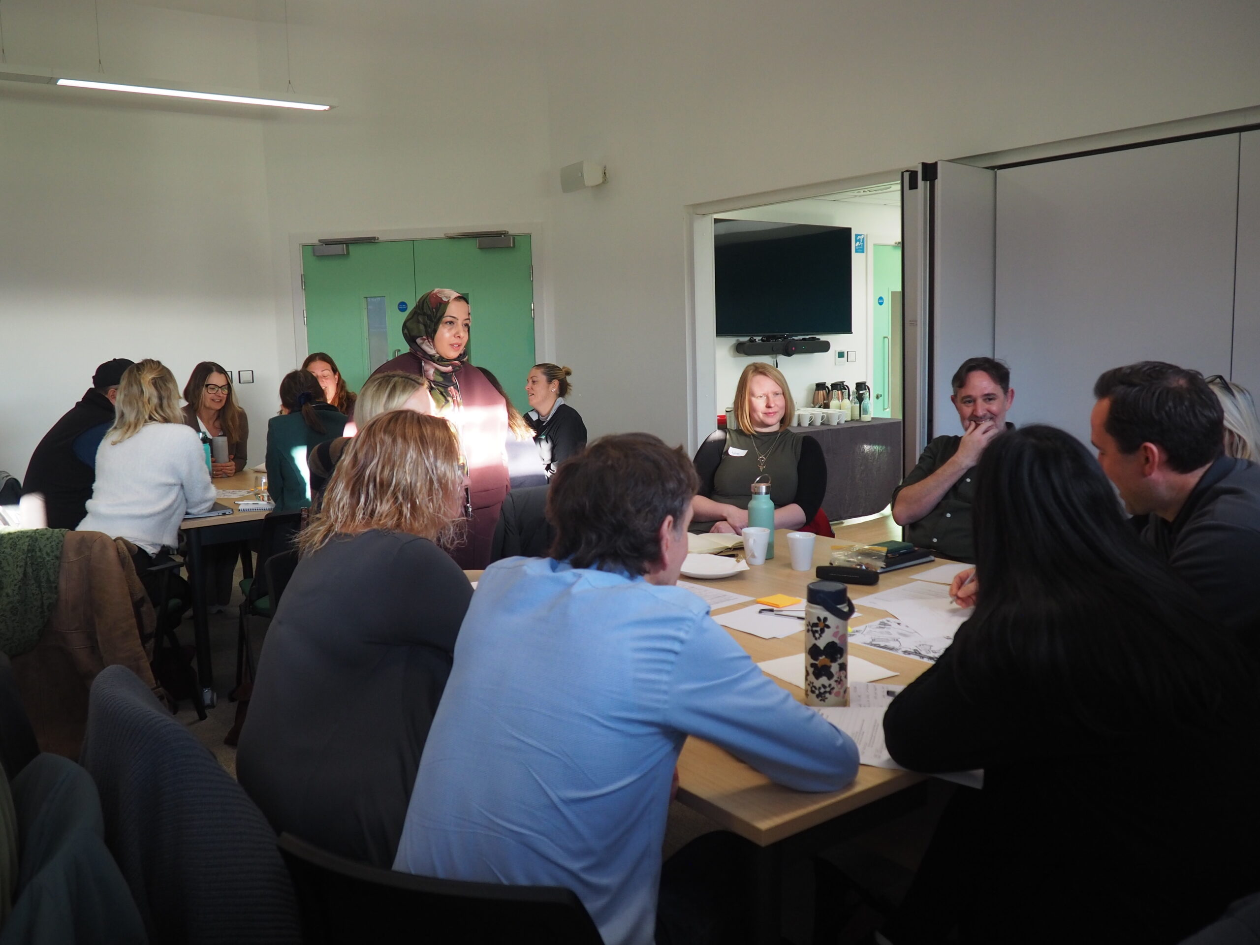 Small groups of partners talking and sharing ideas during an in‑person workshop.