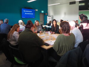 Participants seated at tables taking part in a collaborative workshop with a presentation on screen.