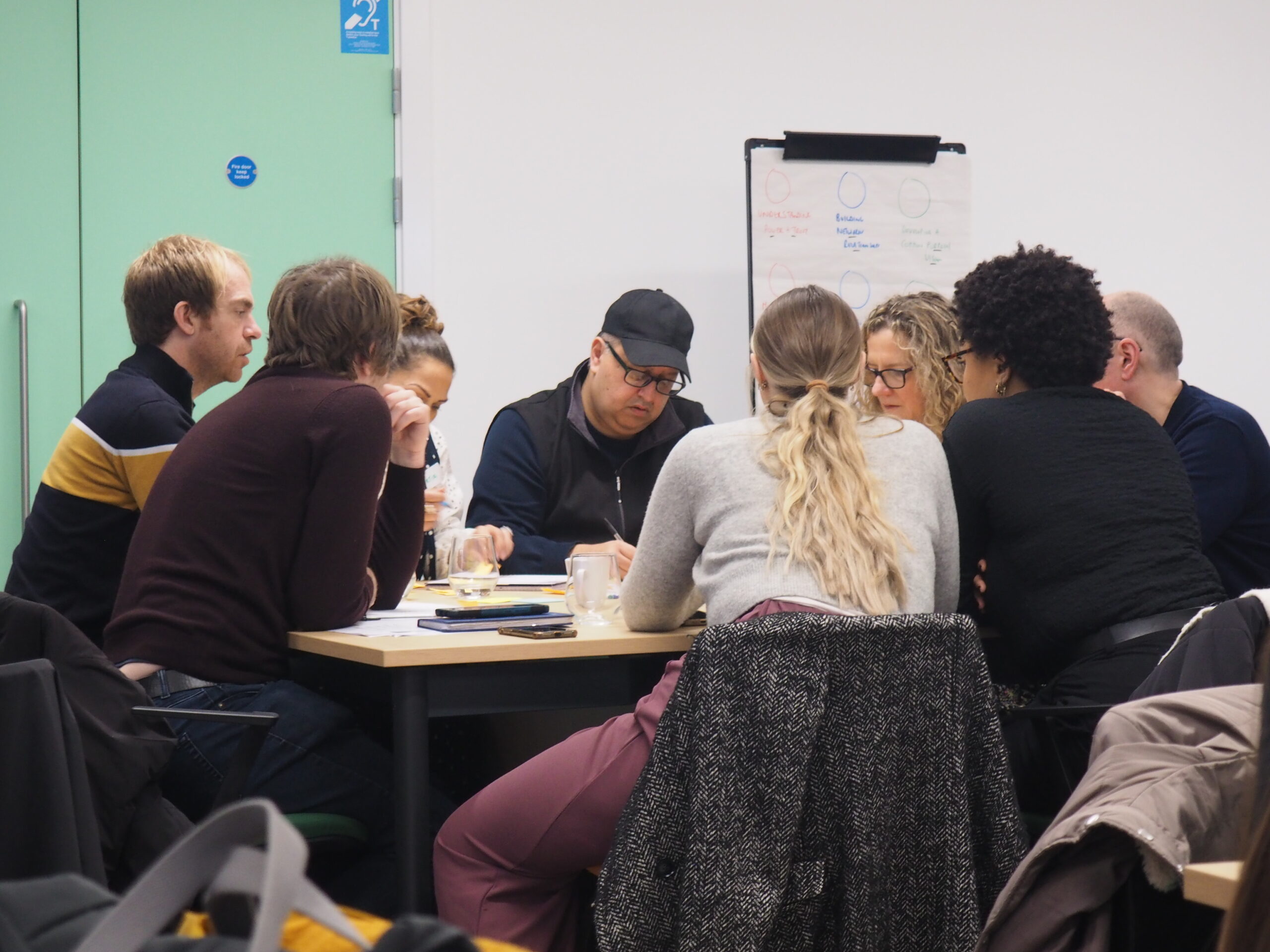 Facilitated group discussion with participants writing and talking together in a meeting room.